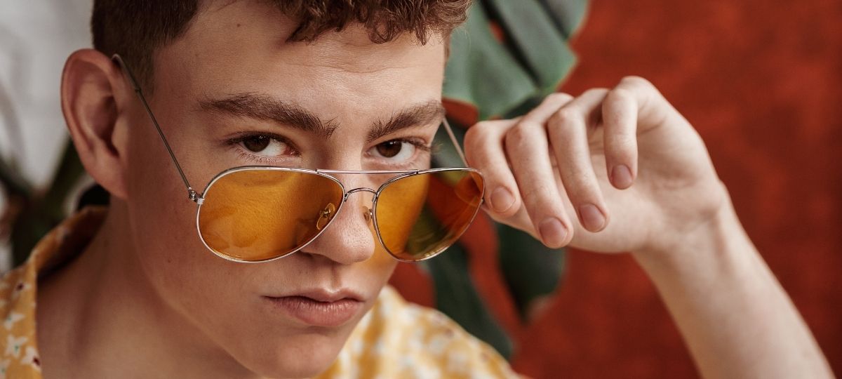 A young man looking at the camera pulling his glasses off his face