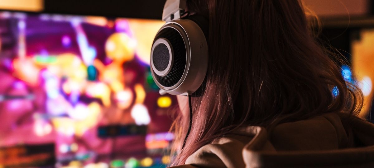 A photo from behind of a woman while looking into a computer monitor with headphones on