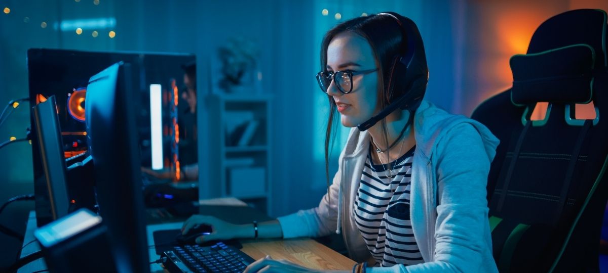 A young woman intensely looking into a computer monitor while in a dark bedroom