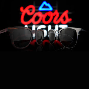 coors glasses sitting in front of a neon coors sign