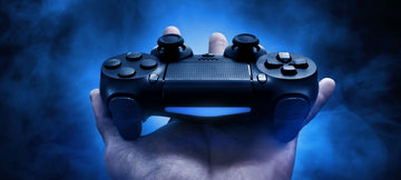 Someone holding a PS4 controller in their hand with a blue-black background shot from the persons point of view