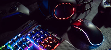 A gaming setup in a dark room lit up with LED lights from a keyboard and mouse